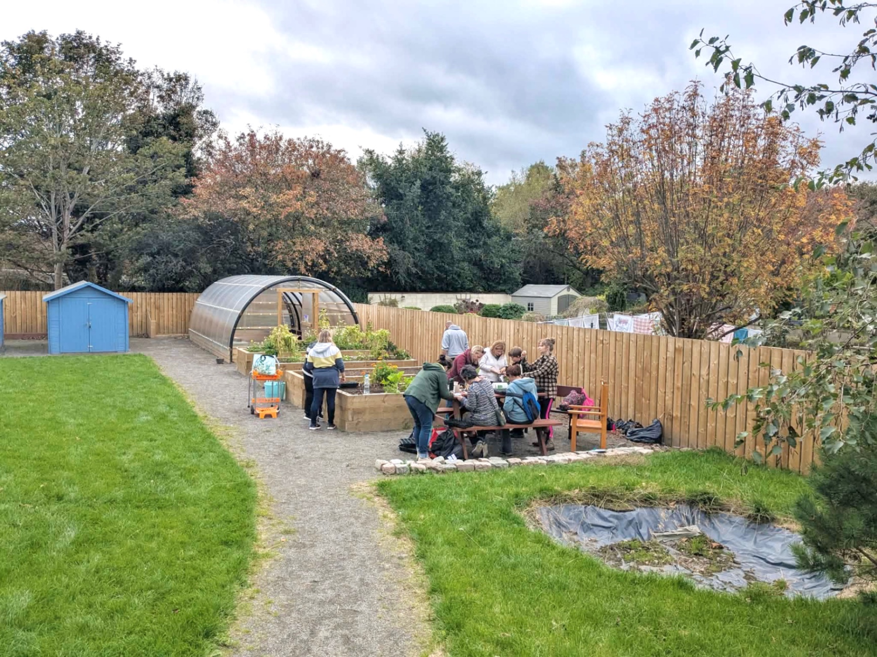 A therapeutic horticulture session at a community garden — raised beds, polytunnel and a group gathered around a wooden table